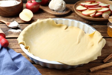 Baking dish with raw dough for apple pie and ingredients on wooden table Photo of Baking dish with raw dough for apple pie and ingredients on wooden table