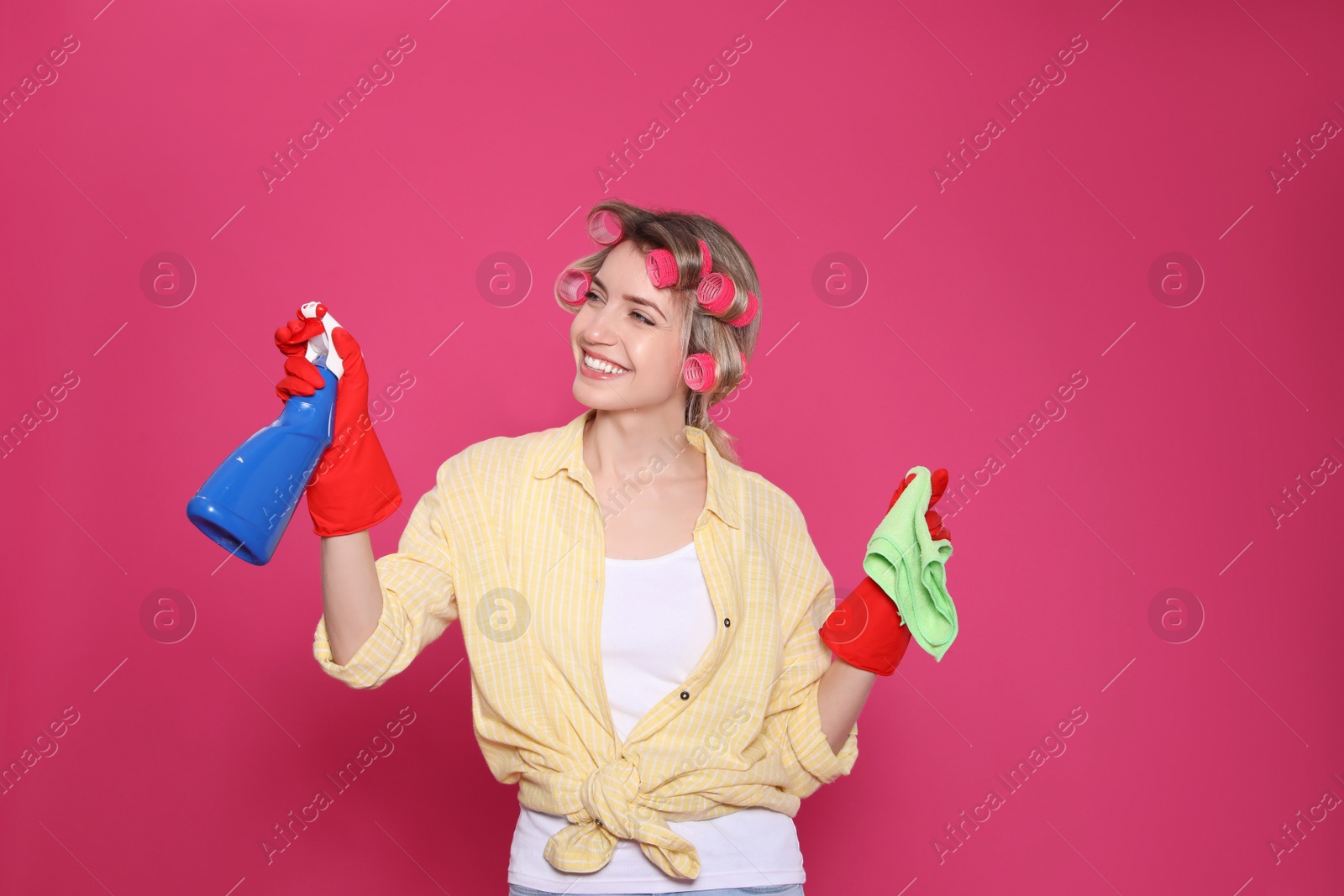 Photo of Young housewife with detergent and rag on pink background