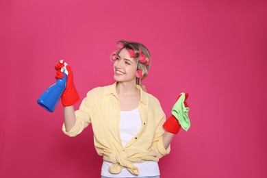 Young housewife with detergent and rag on pink background Photo of Young housewife with detergent and rag on pink background