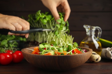 Woman cutting fresh organic microgreen at wooden table, focus on bowl of delicious salad Photo of Woman cutting fresh organic microgreen at wooden table, focus on bowl of delicious salad