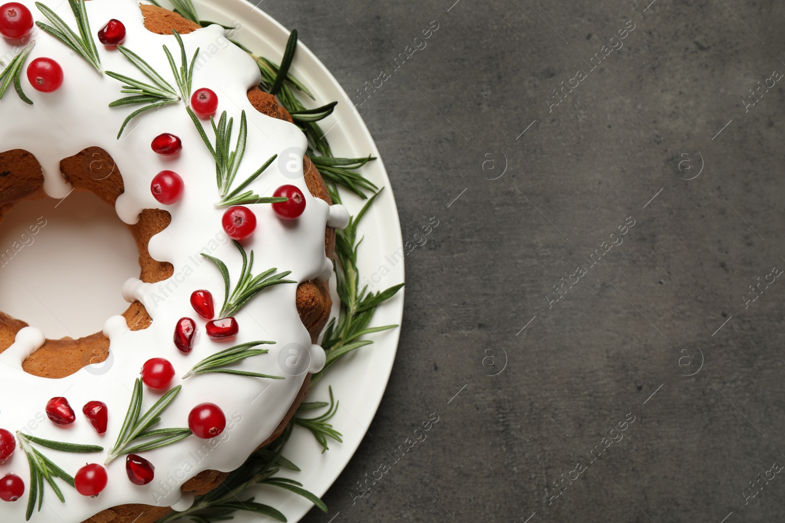 Traditional Christmas cake decorated with glaze, pomegranate seeds, cranberries and rosemary on grey textured table, top view. Space for text Photo of Traditional Christmas cake decorated with glaze, pomegranate seeds, cranberries and rosemary on grey textured table, top view. Space for text