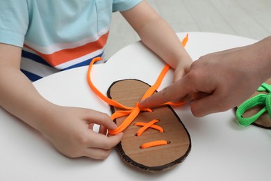 Mother teaching son to tie shoe laces using training cardboard template at white table, closeup Photo of Mother teaching son to tie shoe laces using training cardboard template at white table, closeup