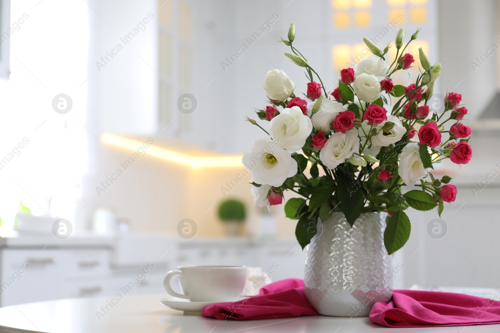 Vase with fresh flowers and cup on table in kitchen. Space for text Photo of Vase with fresh flowers and cup on table in kitchen. Space for text