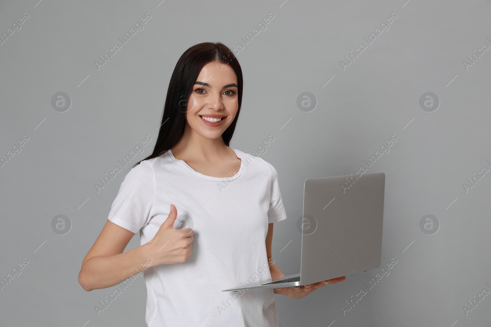 Young woman with modern laptop on light grey background Photo of Young woman with modern laptop on light grey background