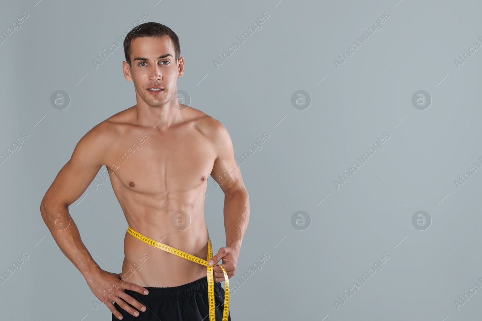 Handsome shirtless man with slim body and measuring tape around his waist on grey background. Space for text Photo of Handsome shirtless man with slim body and measuring tape around his waist on grey background. Space for text