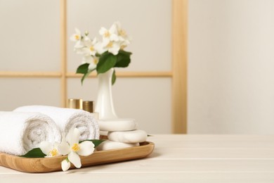 Beautiful jasmine flowers, towels and spa stones on white wooden table, space for text Photo of Beautiful jasmine flowers, towels and spa stones on white wooden table, space for text