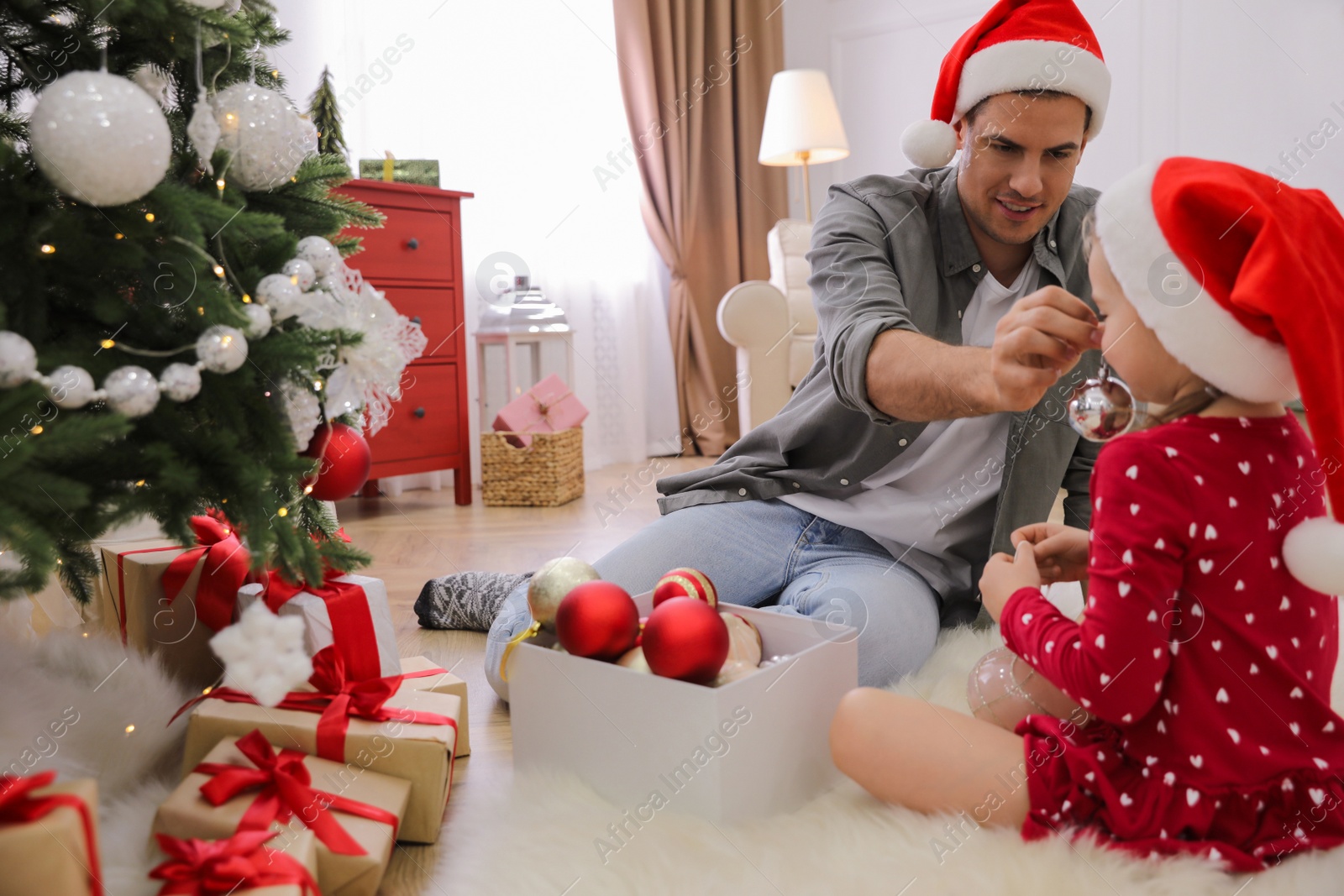 Father with his cute daughter in Santa hats having fun while decorating Christmas tree at home Photo of Father with his cute daughter in Santa hats having fun while decorating Christmas tree at home