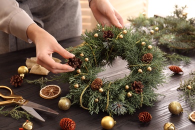 Florist making beautiful Christmas wreath at wooden table indoors, closeup Photo of Florist making beautiful Christmas wreath at wooden table indoors, closeup