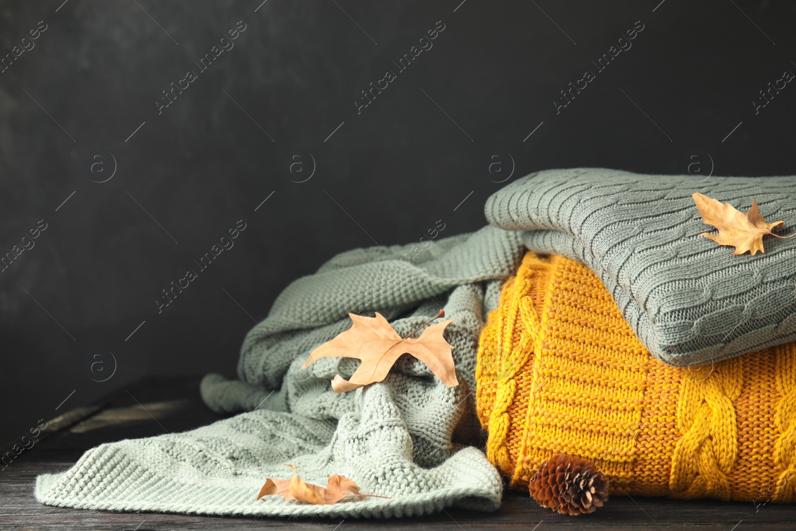 Different soft plaids, dry leaves and fir cone on black wooden table, closeup Photo of Different soft plaids, dry leaves and fir cone on black wooden table, closeup