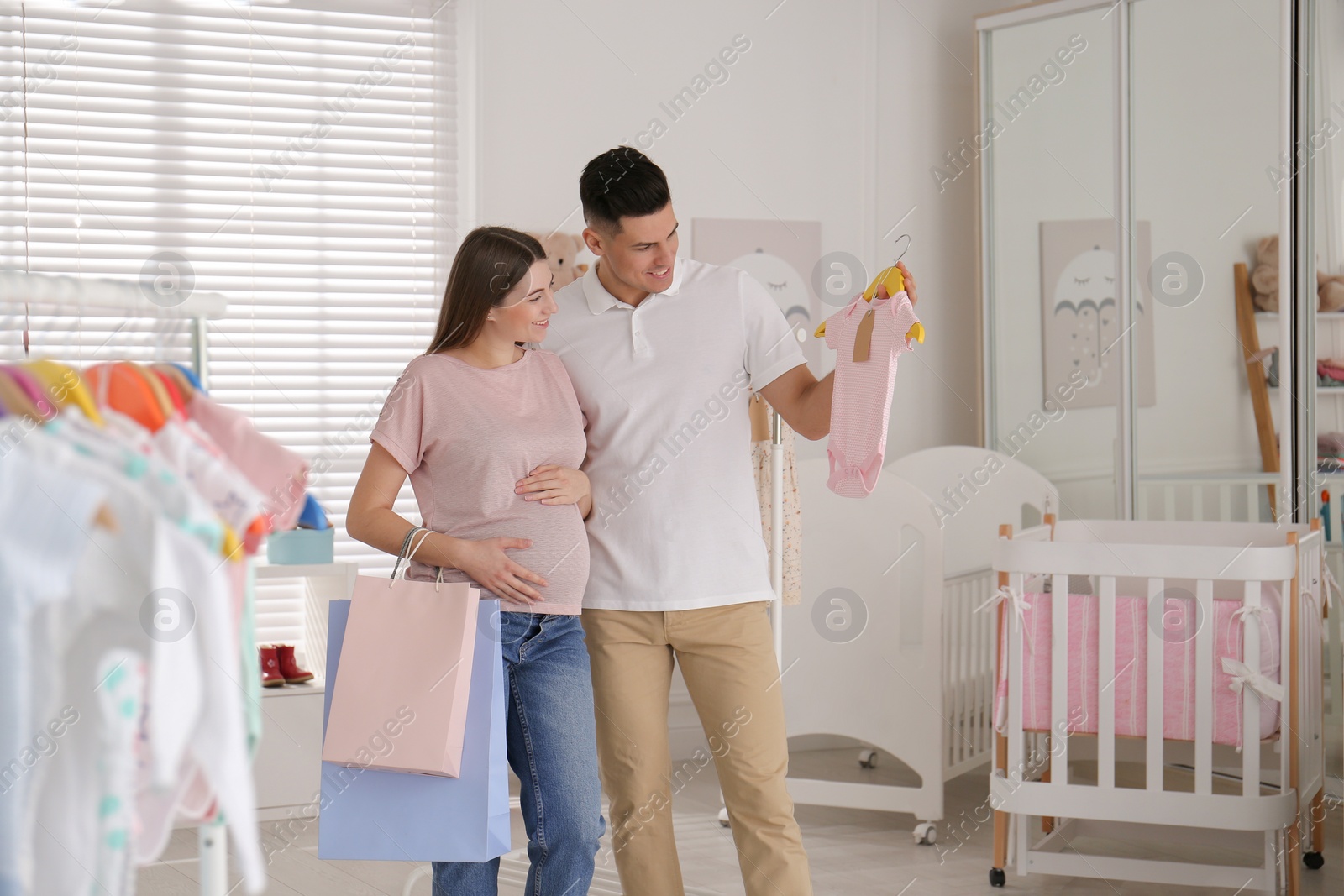 Photo of Happy pregnant woman with her husband choosing baby clothes in store. Shopping concept
