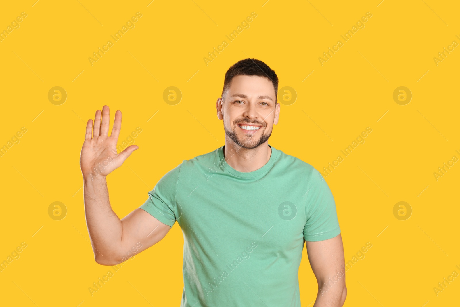 Cheerful man waving to say hello on yellow background Photo of Cheerful man waving to say hello on yellow background