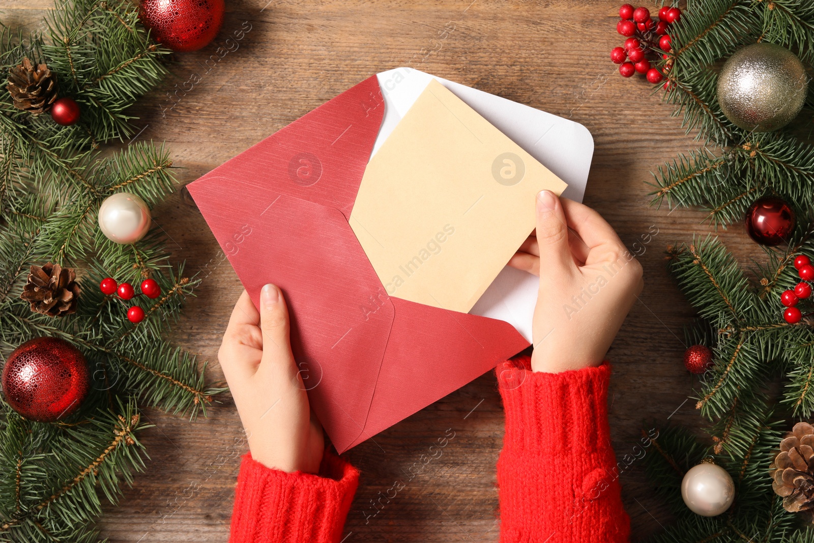 Photo of Woman taking blank Christmas card from envelope at wooden table, top view with space for text