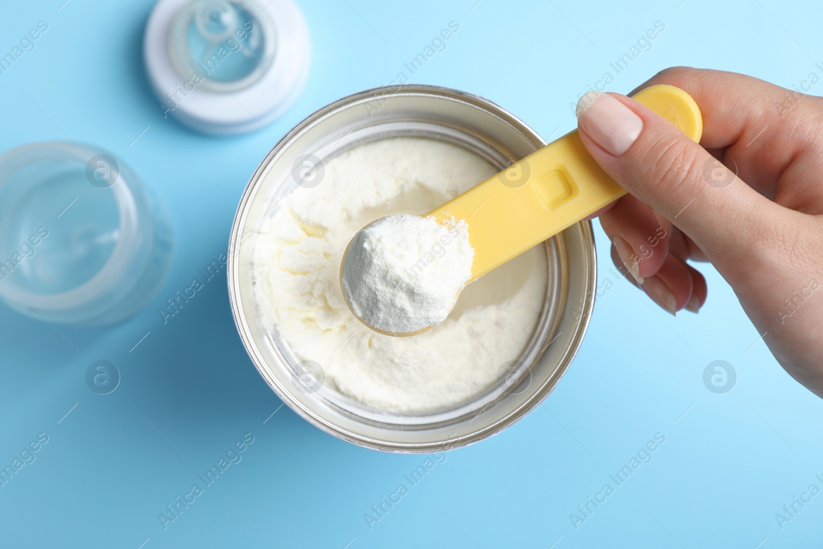 Woman taking powdered infant formula with scoop from can on light blue background, top view Photo of Woman taking powdered infant formula with scoop from can on light blue background, top view