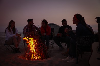 Group of friends gathering around bonfire on beach in evening. Camping season Photo of Group of friends gathering around bonfire on beach in evening. Camping season