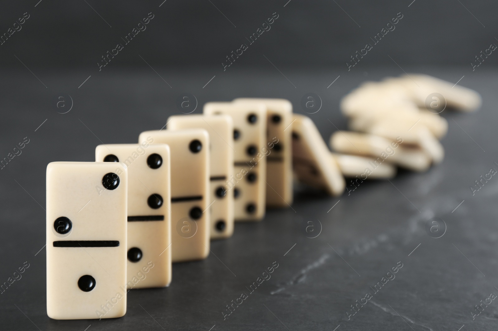 White domino tiles falling on dark grey table Photo of White domino tiles falling on dark grey table