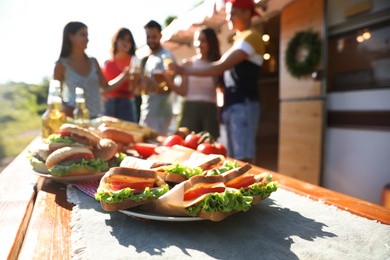 Friends toasting with bottles of drinks near motorhome, focus on table full of tasty food. Camping season Photo of Friends toasting with bottles of drinks near motorhome, focus on table full of tasty food. Camping season