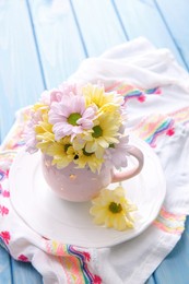 Bouquet of beautiful flowers in cup on light blue wooden table Photo of Bouquet of beautiful flowers in cup on light blue wooden table