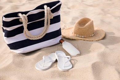 Beach bag, flip flops, sunscreen and hat on sand Photo of Beach bag, flip flops, sunscreen and hat on sand