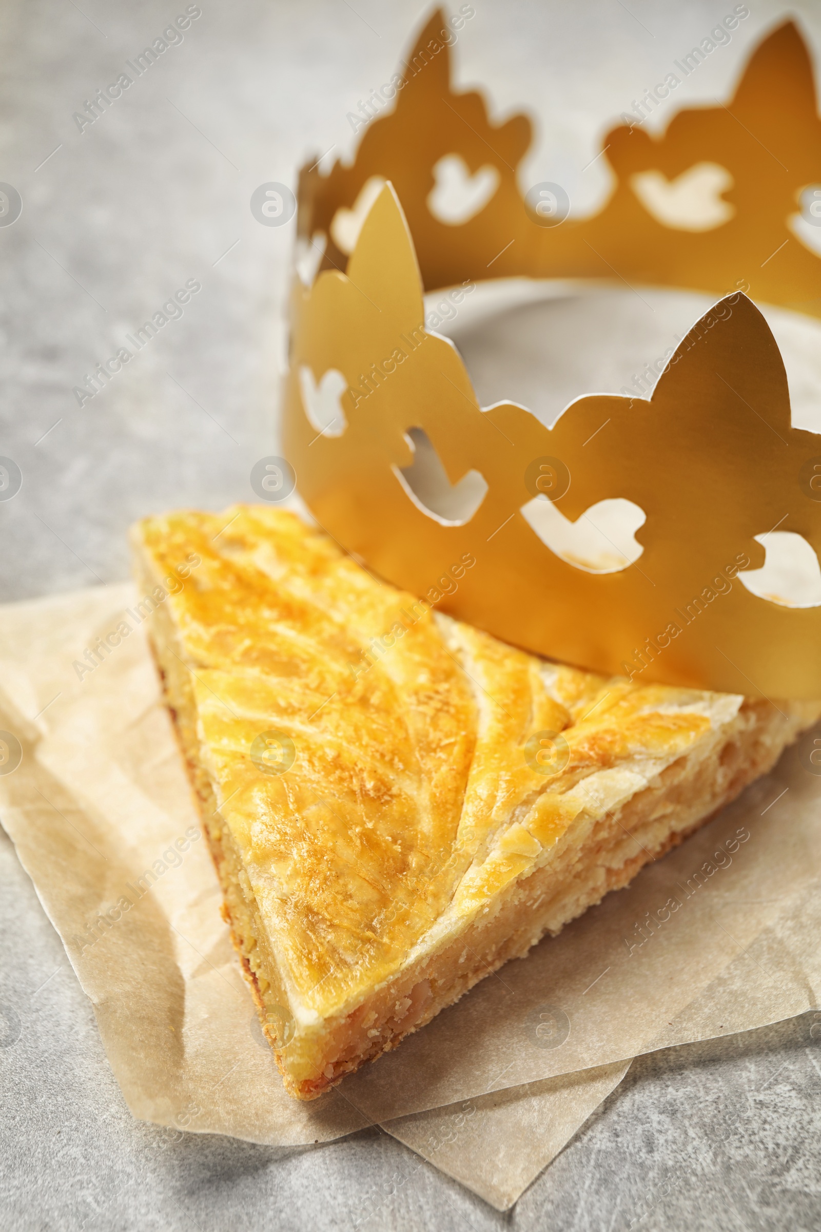 Slice of traditional galette des Rois with paper crown on light grey table, closeup Photo of Slice of traditional galette des Rois with paper crown on light grey table, closeup