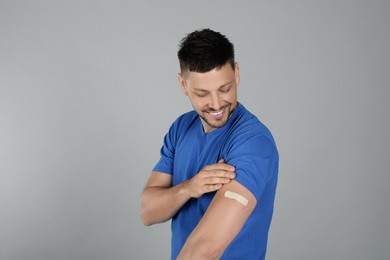 Vaccinated man with medical plaster on his arm against grey background Photo of Vaccinated man with medical plaster on his arm against grey background