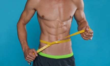 Shirtless man with slim body and measuring tape around his waist on light blue background, closeup Photo of Shirtless man with slim body and measuring tape around his waist on light blue background, closeup