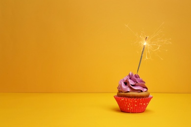 Birthday cupcake with sparkler on color background Photo of Birthday cupcake with sparkler on color background