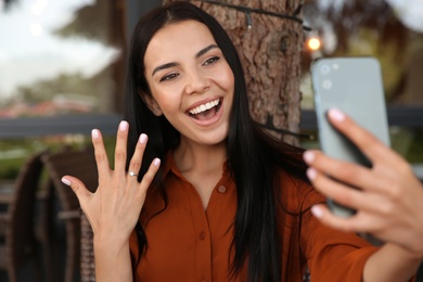 Happy woman with engagement ring taking selfie in outdoor cafe Photo of Happy woman with engagement ring taking selfie in outdoor cafe
