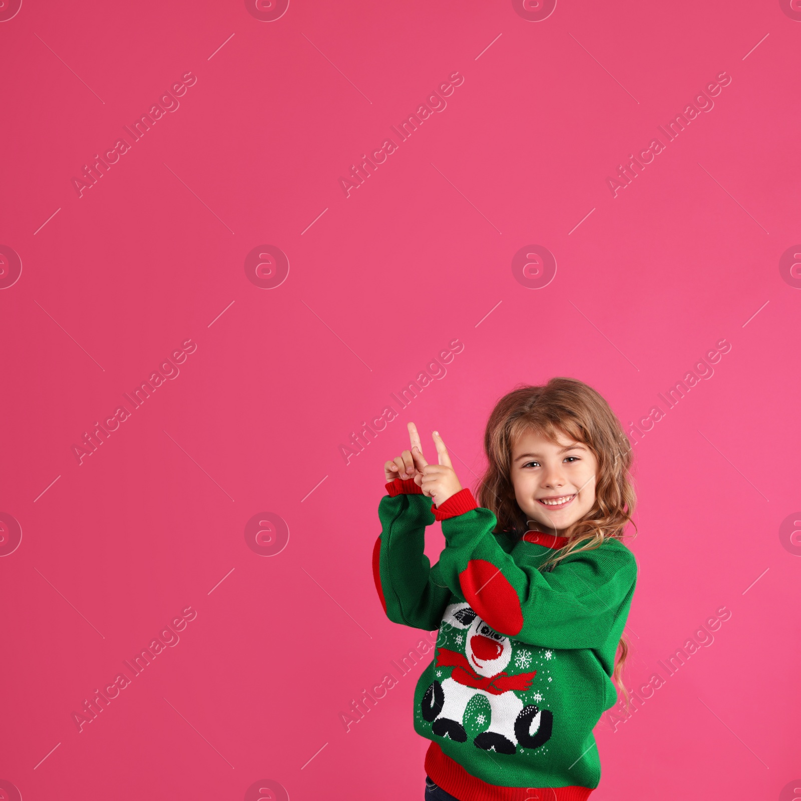 Cute little girl in green Christmas sweater pointing against pink background. Space for text Photo of Cute little girl in green Christmas sweater pointing against pink background. Space for text