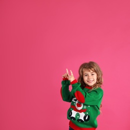 Cute little girl in green Christmas sweater pointing against pink background. Space for text Photo of Cute little girl in green Christmas sweater pointing against pink background. Space for text