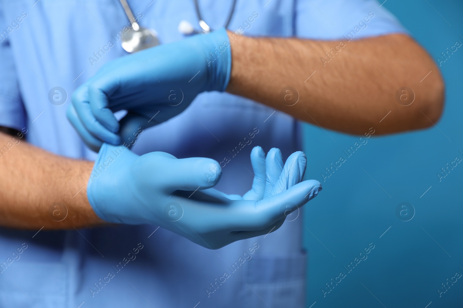 Doctor putting on medical gloves against blue background, closeup Photo of Doctor putting on medical gloves against blue background, closeup