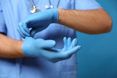 Photo of Doctor putting on medical gloves against blue background, closeup