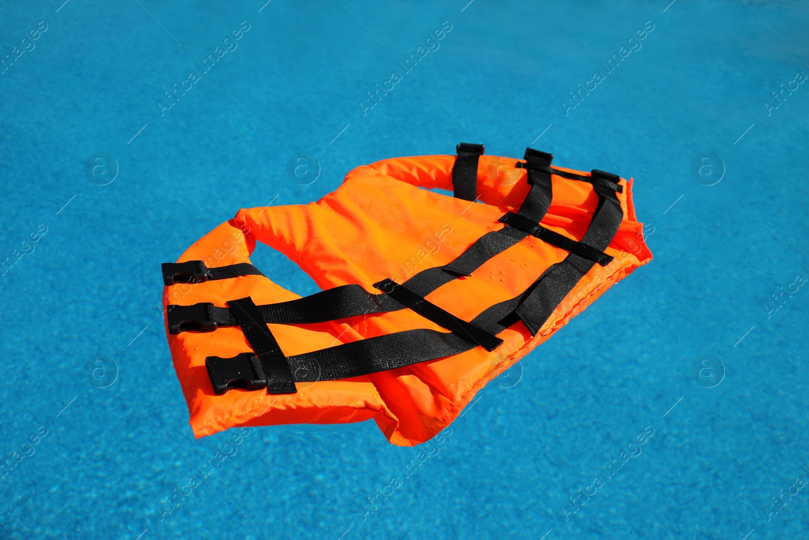 Bright orange life jacket floating in swimming pool Photo of Bright orange life jacket floating in swimming pool