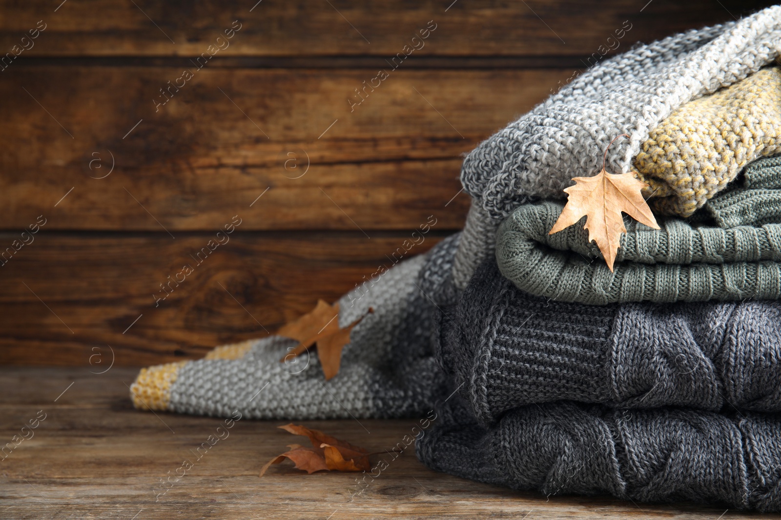 Stack of knitted plaids with dry leaves on wooden table, closeup Photo of Stack of knitted plaids with dry leaves on wooden table, closeup