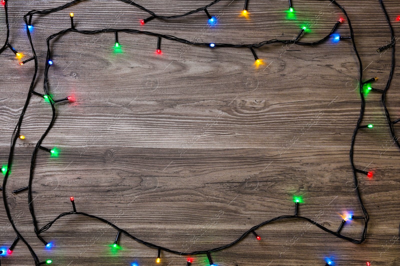 Frame of Christmas lights on wooden table, top view. Space for text Photo of Frame of Christmas lights on wooden table, top view. Space for text