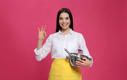 Young housewife with pan on pink background Photo of Young housewife with pan on pink background