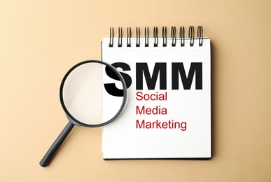 Notebook with text SMM (Social media marketing) and magnifier glass on beige background, flat lay Image of Notebook with text SMM (Social media marketing) and magnifier glass on beige background, flat lay