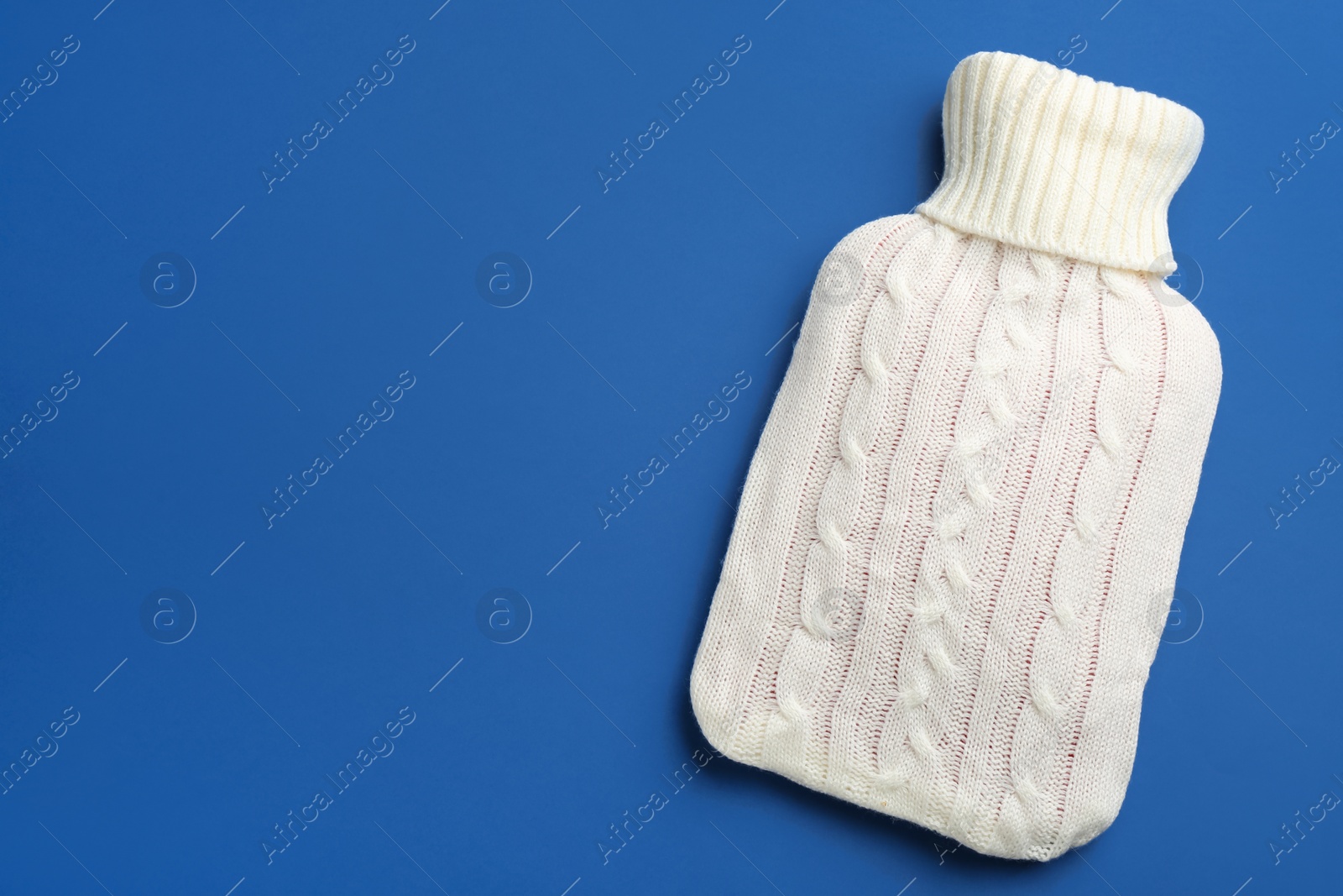 Photo of Hot water bottle with knitted cover on blue background, top view. Space for text