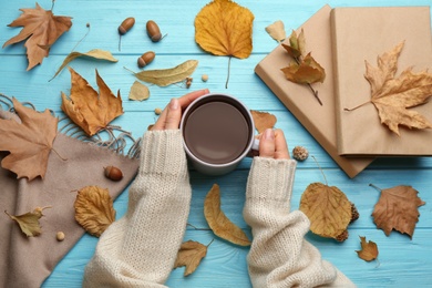 Woman with cup of hot drink at light blue wooden table, top view. Cozy autumn atmosphere Photo of Woman with cup of hot drink at light blue wooden table, top view. Cozy autumn atmosphere