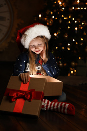 Cute child opening magic gift box near Christmas tree at night Photo of Cute child opening magic gift box near Christmas tree at night