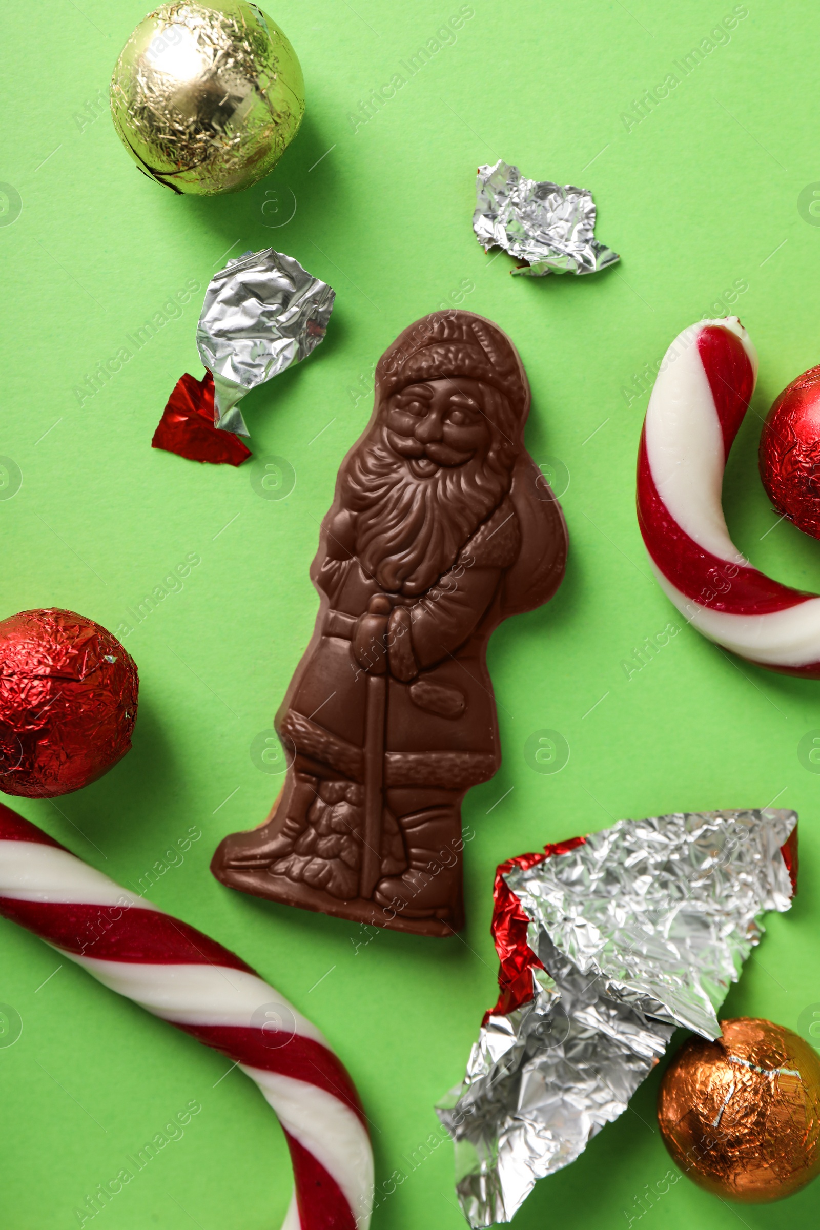Chocolate Santa Claus among sweets on light green background, flat lay Photo of Chocolate Santa Claus among sweets on light green background, flat lay