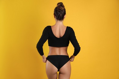 Woman in black sexy panties on yellow background, back view Photo of Woman in black sexy panties on yellow background, back view