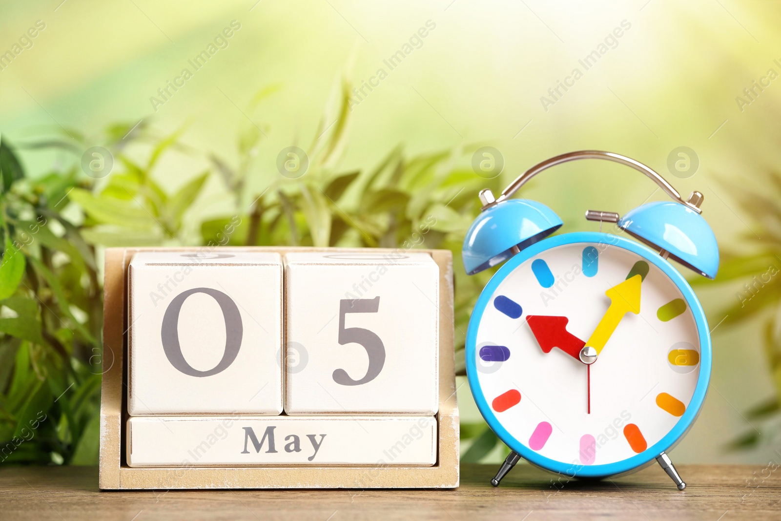 Wooden block calendar and alarm clock on table against blurred green background Image of Wooden block calendar and alarm clock on table against blurred green background