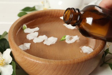 Woman pouring jasmine essential oil into bowl with petals at table, closeup Photo of Woman pouring jasmine essential oil into bowl with petals at table, closeup