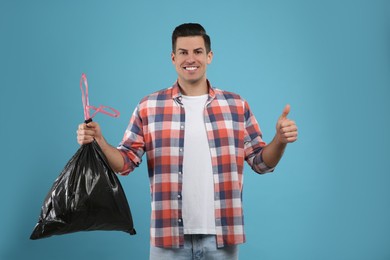 Man holding full garbage bag on light blue background Photo of Man holding full garbage bag on light blue background