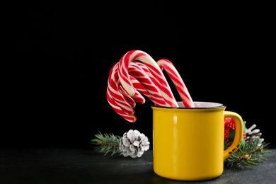 Christmas candy canes in cup on black table against dark background, space for text Photo of Christmas candy canes in cup on black table against dark background, space for text