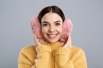 Photo of Beautiful young woman wearing earmuffs on light grey background