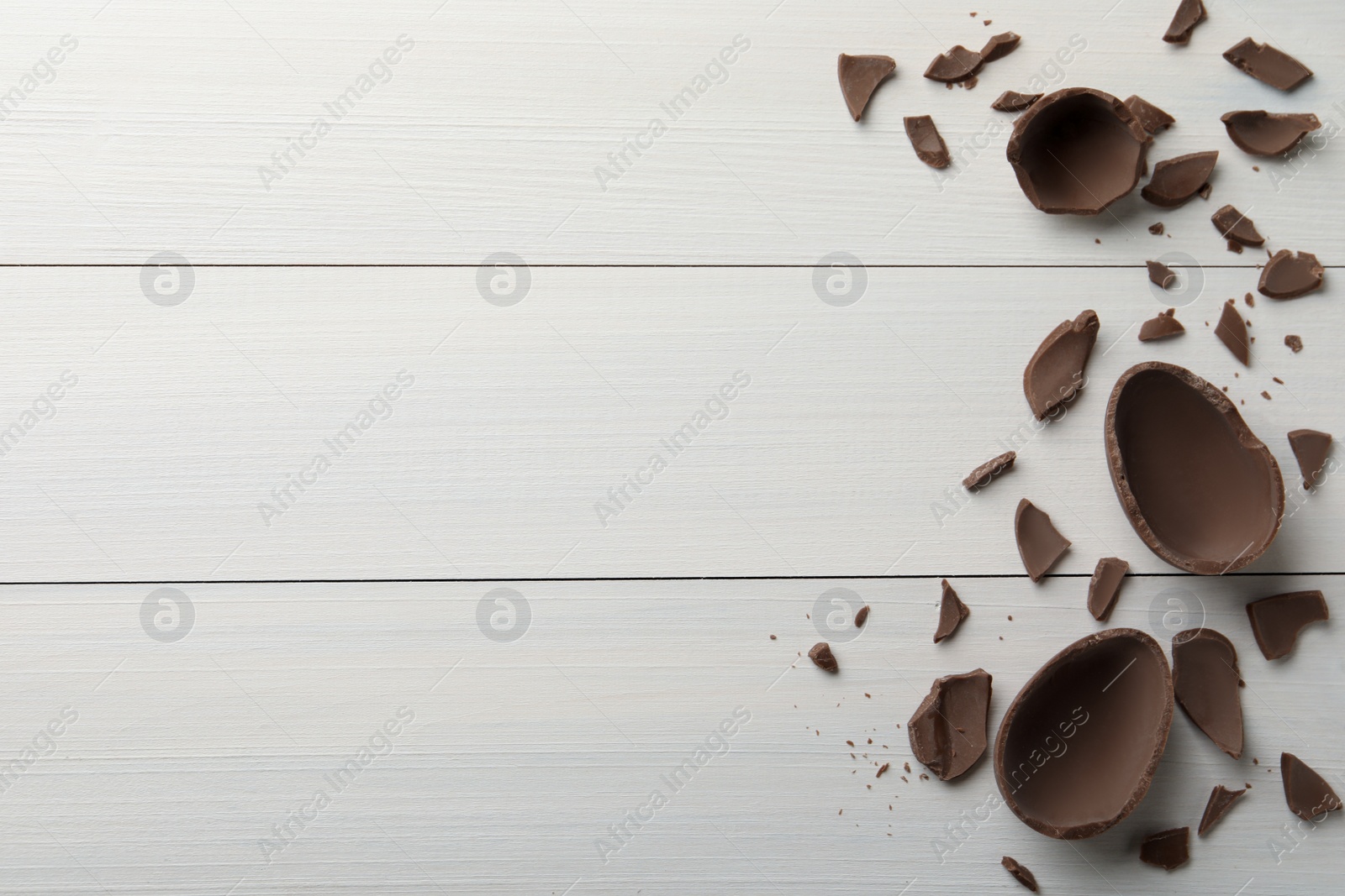 Broken chocolate egg on white wooden table, flat lay. Space for text Photo of Broken chocolate egg on white wooden table, flat lay. Space for text