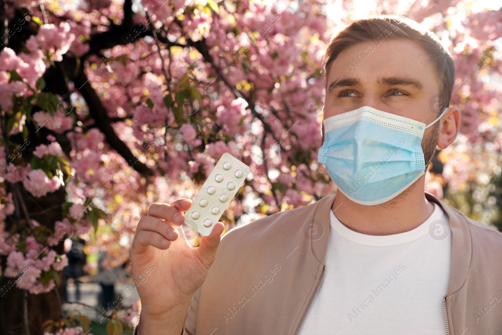 Man with pills and protective mask near blossoming tree outdoors. Seasonal pollen allergy Photo of Man with pills and protective mask near blossoming tree outdoors. Seasonal pollen allergy