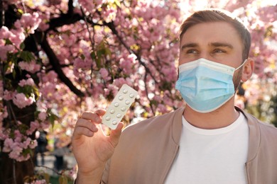 Man with pills and protective mask near blossoming tree outdoors. Seasonal pollen allergy Photo of Man with pills and protective mask near blossoming tree outdoors. Seasonal pollen allergy