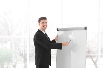 Business trainer giving presentation on flip chart board indoors Photo of Business trainer giving presentation on flip chart board indoors
